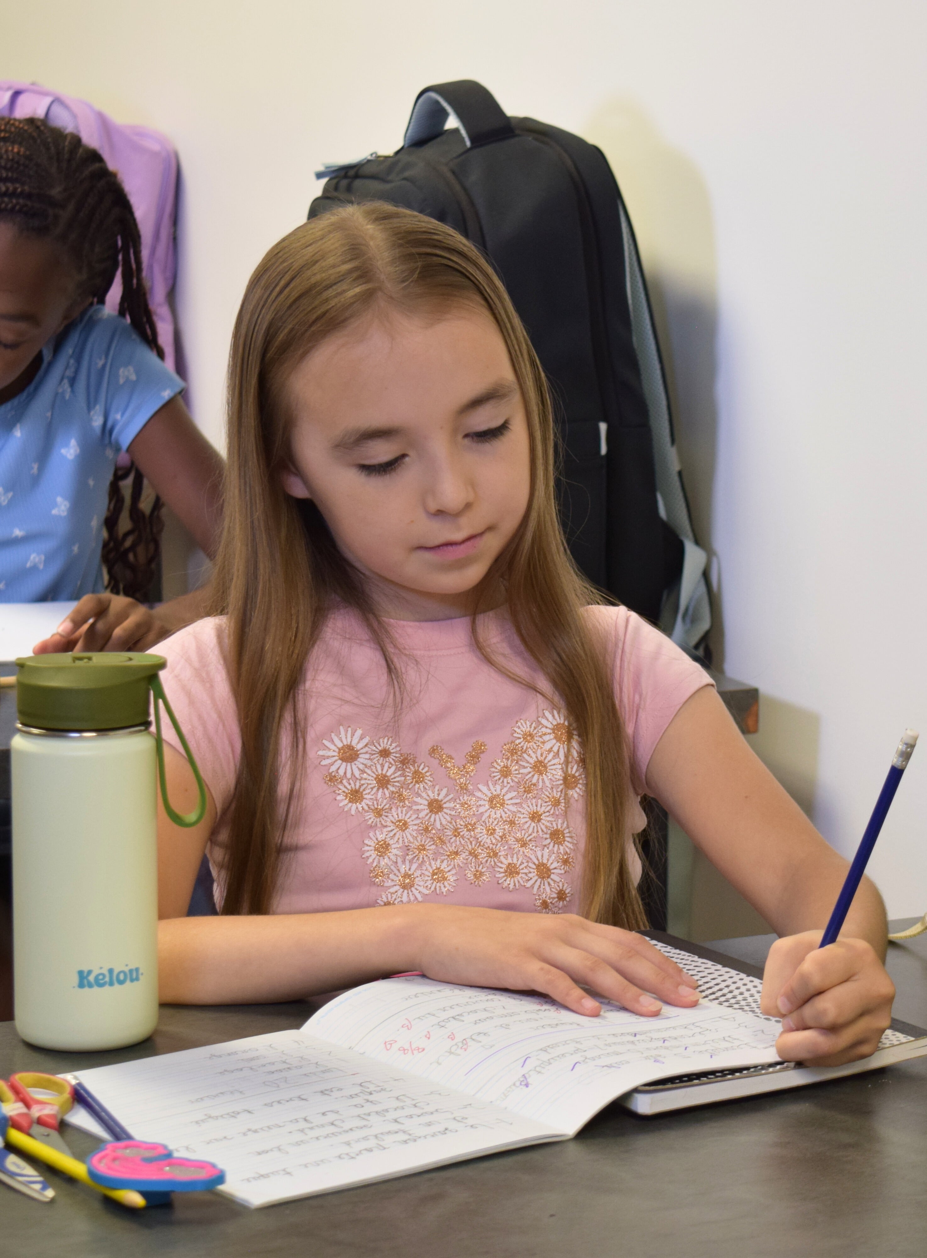 Girl writing in a notebook with a water bottle and backpack in the background