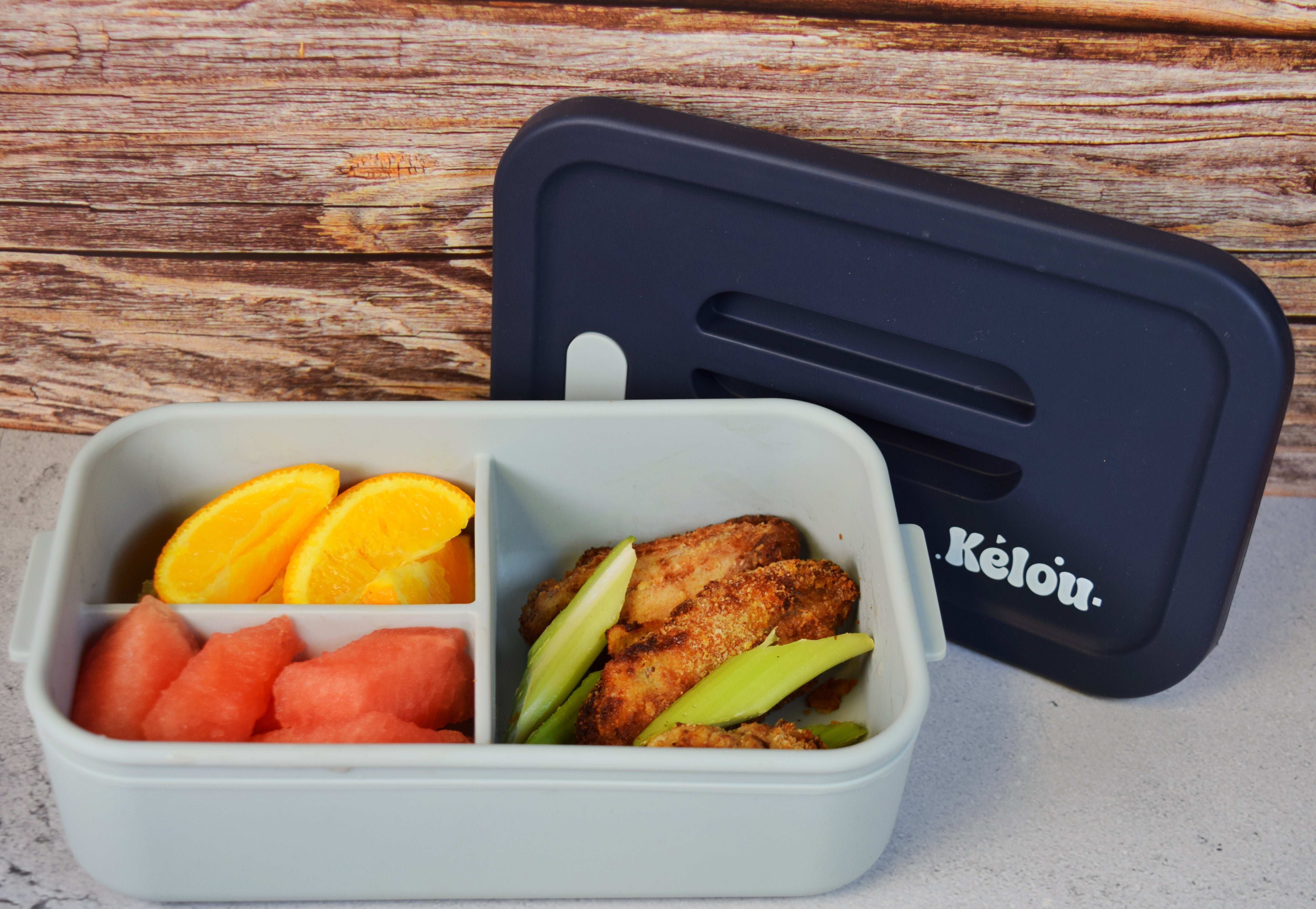 Bento box with compartments of food and a black lid on a wooden surface