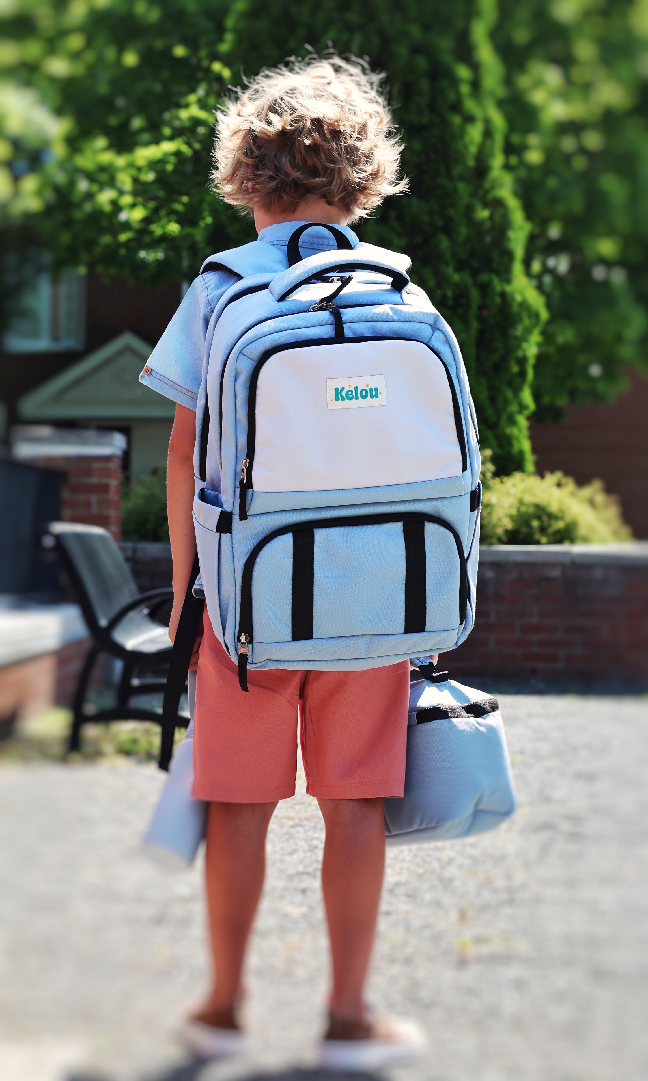 Child wearing a blue and gray backpack with 'Kelou' branding outdoors.