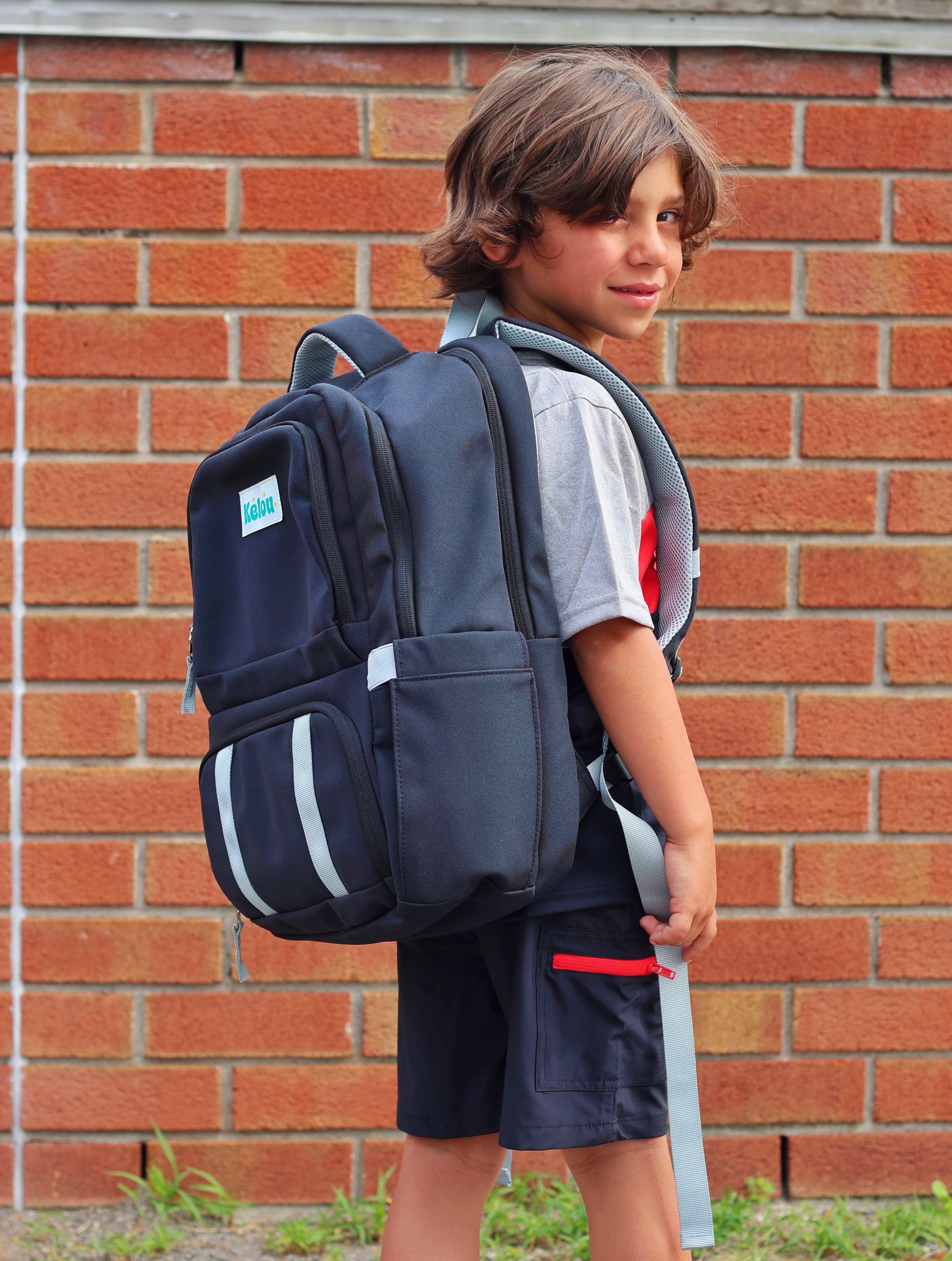 Child wearing a large backpack in front of a brick wall